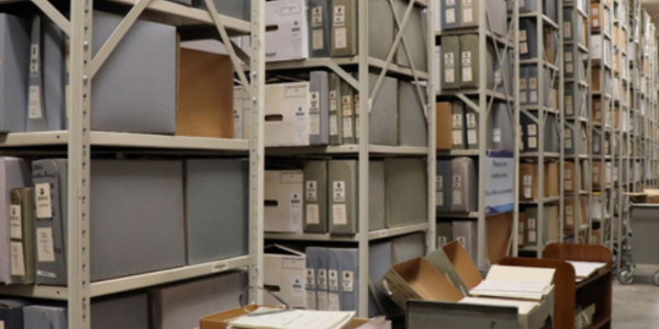 Rows of shelves stacked floor to ceiling with binders and boxes of paper environmental data records extend down a long room in the basement of NCEI headquarters in Asheville, NC.