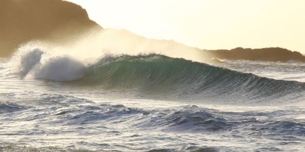 Waves crashing on beach cliffs during sunrise. 