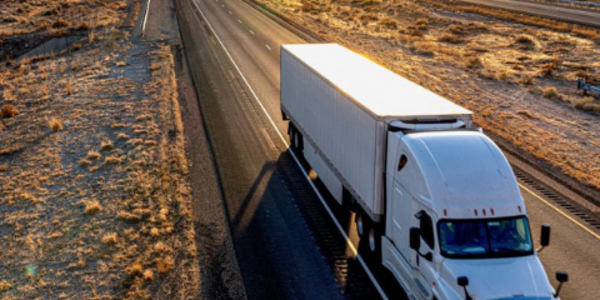 Semi driving on a road through the desert with mountains in the background