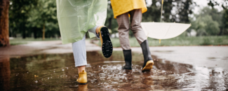 Two people in rainboots with a white umbrella going through puddles. Two people in rainboots with a white umbrella going through puddles.