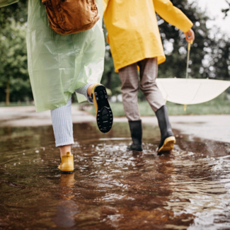 Two people in rainboots with a white umbrella going through puddles.