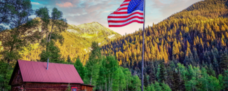 Yellow tree foliage on the mountains with a cabin and an American flag in the forefront.