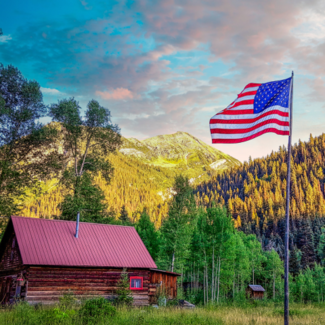 Yellow tree foliage on the mountains with a cabin and an American flag in the forefront.