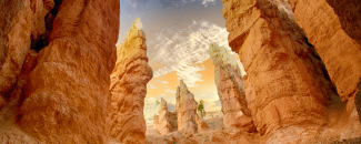 Canyon desert landscape with the sun setting in yellow and orange hues overhead. Canyon desert landscape with the sun setting in yellow and orange hues overhead.