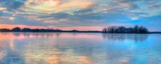 Blue, orange, and yellow sunset over a large body of water with a skyline of trees in the background. Blue, orange, and yellow sunset over a large body of water with a skyline of trees in the background.