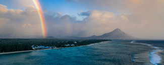 Rainbow on the left amidst a haze of dark clouds, the ocean, and mountains in the background. Rainbow on the left amidst a haze of dark clouds, the ocean, and mountains in the background.