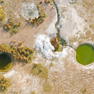 Desiccated landscape with two large holes in the land filled with green tinted water.