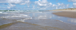 Tide receding from sandy shore with blue sky and clouds overhead Tide receding from sandy shore with blue sky and clouds overhead
