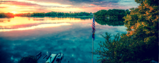 An American flag on a pole in front of a lake at sundown. An American flag on a pole in front of a lake at sundown.