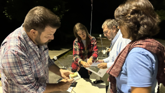 Alt text: Image of four Asheville GreenWorks staff and volunteers gathered around a table in the early morning hours planning their driving routes for the day. (Credit: Asheville GreenWorks)