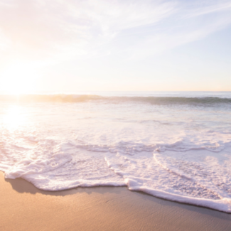 A wave breaking upon a shore with the sun low on the horizon.