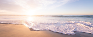 A wave breaking upon a shore with the sun low on the horizon. A wave breaking upon a shore with the sun low on the horizon.