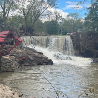 A rain-swollen Reems Creek in Weaverville, NC in the aftermath of Hurricane Helene. The remnants of a red water wheel and other debris lie along the side of the falls. 