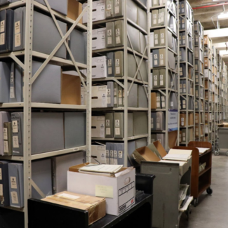 Rows of shelves stacked floor to ceiling with binders and boxes of paper environmental data records extend down a long room in the basement of NCEI headquarters in Asheville, NC.