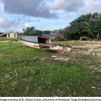 A damaged boat washed up into the middle of a field in front of a hut.