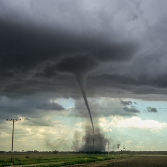 A tornado approaching an open field with a tinge of blue sky in the background.