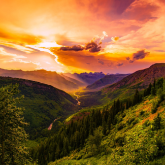The sun setting behind clouds over a valley.
