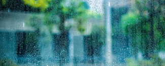Rain flecked on a windowpane with trees and buildings visible through the glass. Rain flecked on a windowpane with trees and buildings visible through the glass.