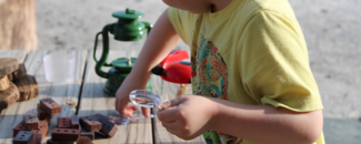 Child using magnifying glass at picnic table covered in toys.